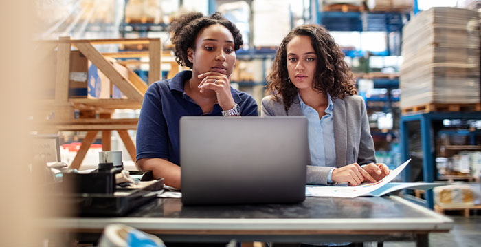 Two women looking at reports on a computer inside a warehouse