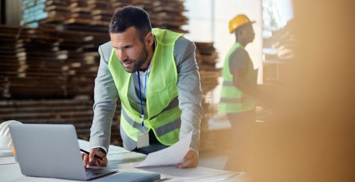 A worker calculates the weighted average cost on a laptop in a warehouse.