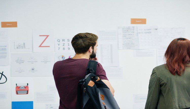 man and woman looking at papers posted on a white wall