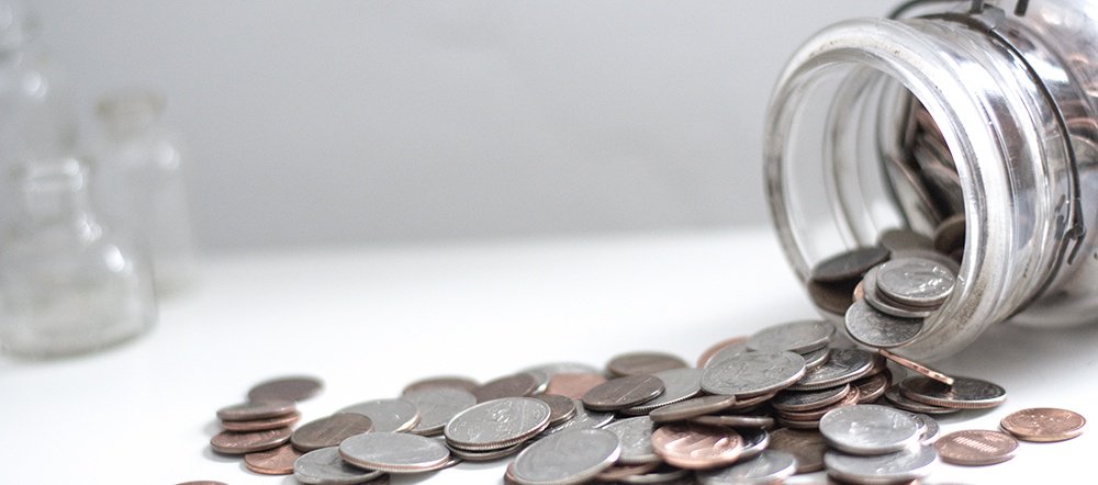 glass jar with many coins spilling out of it