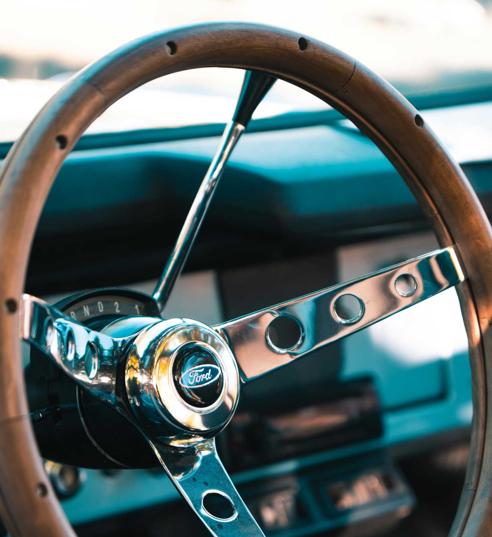 Close-up view of a vintage car steering wheel with a metallic finish and wooden rim inside a classic vehicle.