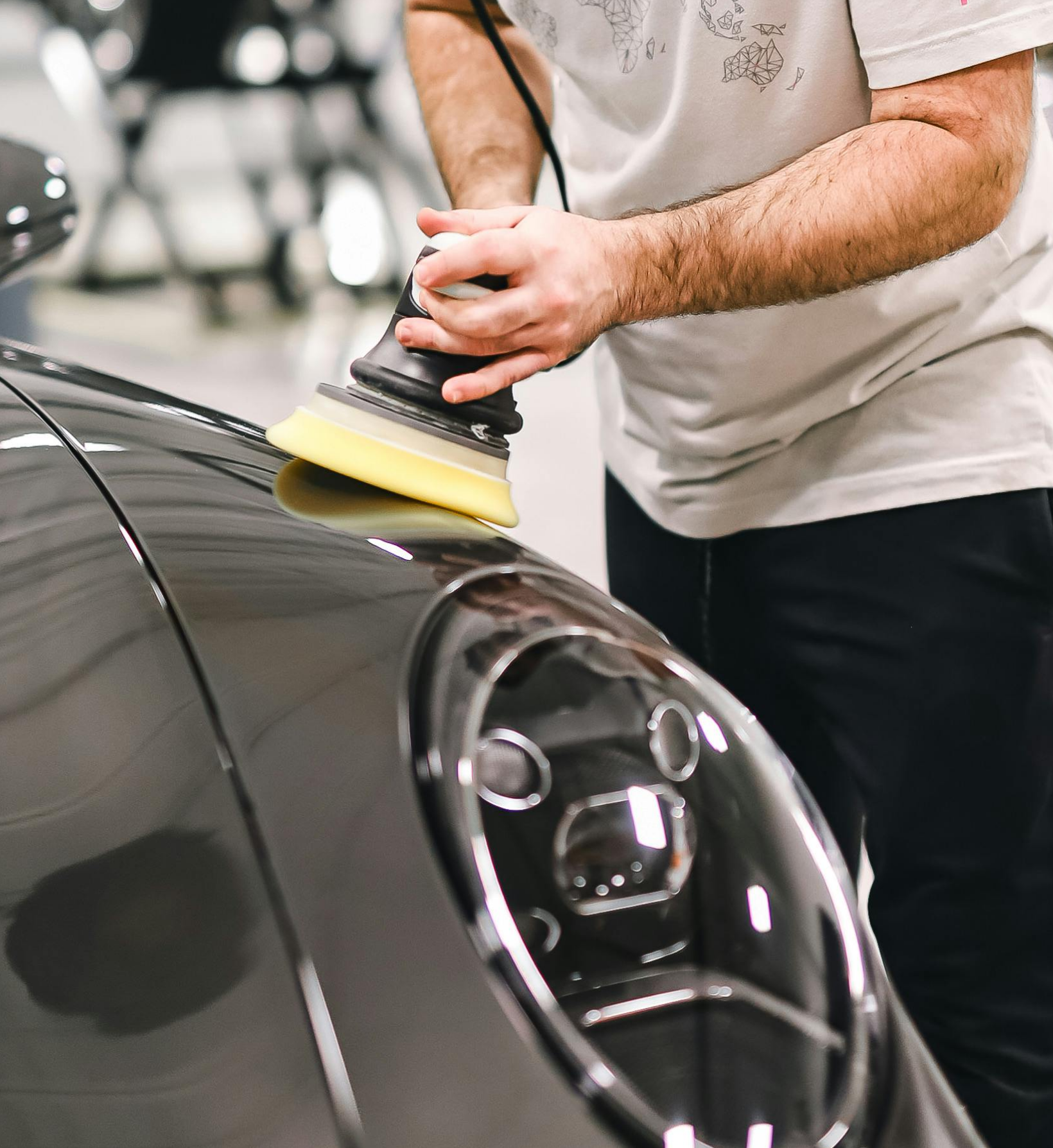 Person polishing the hood of a black car with a power buffer during auto detailing.
